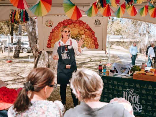 A speak with short blonde hair and glasses speaking at an outdoor event for The Root Cause, a 2024 RASF Charity Brunch recipient.