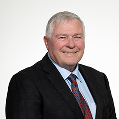 Headshot of RASF Board Member Bruce Paynter wearing a dark suit, light blue shirt, and patterned tie, smiling against a plain background.