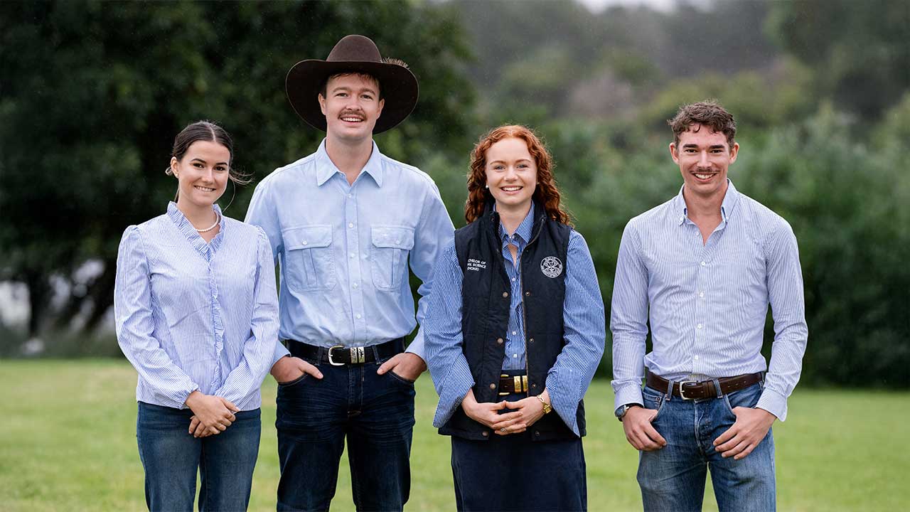 Four young adults - the RAS Foundation Rural Scholarship recipients - standing on grass in rural setting, wearing casual work wear.