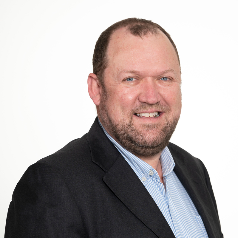 Headshot of Wine Committee Chair and Board Member Angus Barnes, smiling and wearing a dark suit jacket and light blue shirt.