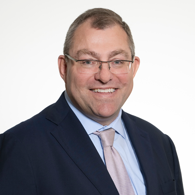 Headshot of Ringmaster and Board Member James Angus, smiling and wearing a dark suit and light pink tie with a blue shirt.