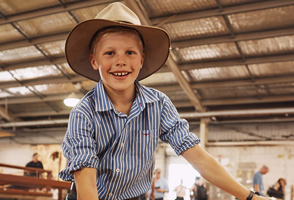 Smiling boy in a striped shirt and wide-brimmed hat standing inside a show pavilion.