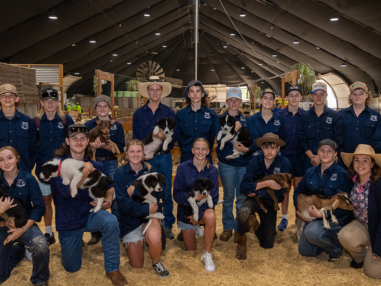 Students from All Roads to the Royal in navy shirts posing inside a barn, each holding a puppy or small animal.