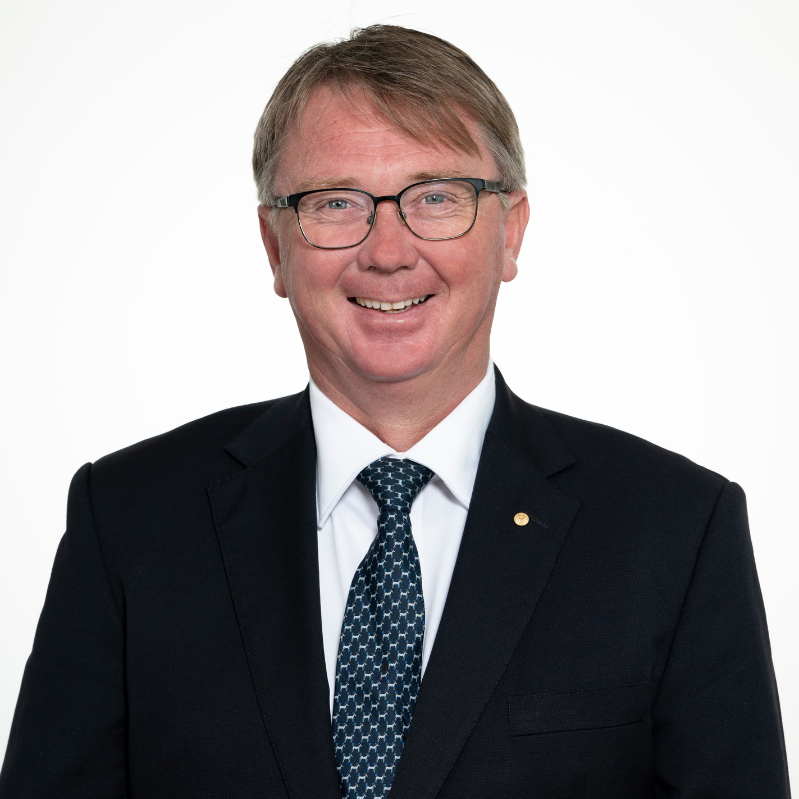 Headshot of President John Bennett OAM, smiling and wearing a dark suit, white shirt, and patterned tie.