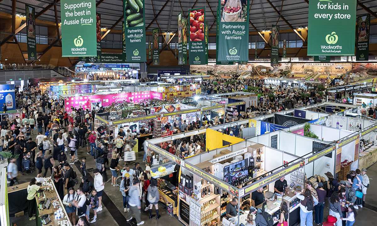 Large crowd exploring exhibition stalls inside the Dome decorated with bright sponsor banners, at the Sydney Royal Easter Show.