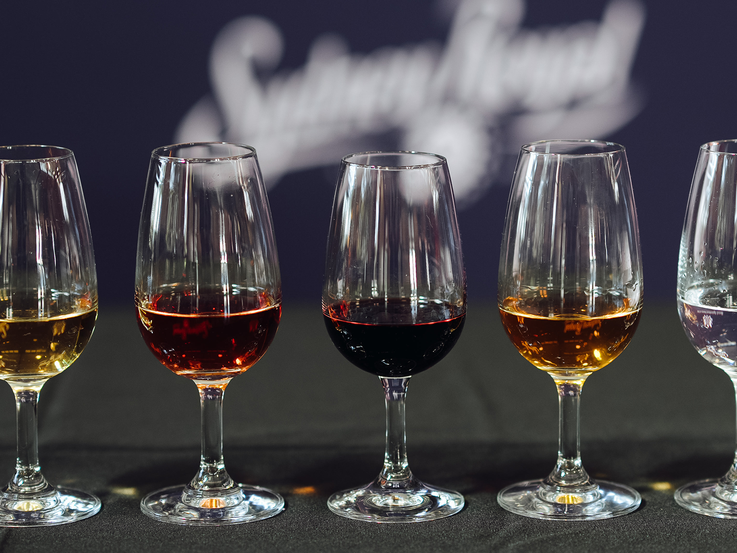 Glasses of golden, amber, and dark spirits on a black table at the Sydney Royal Distilled Spirits Show.