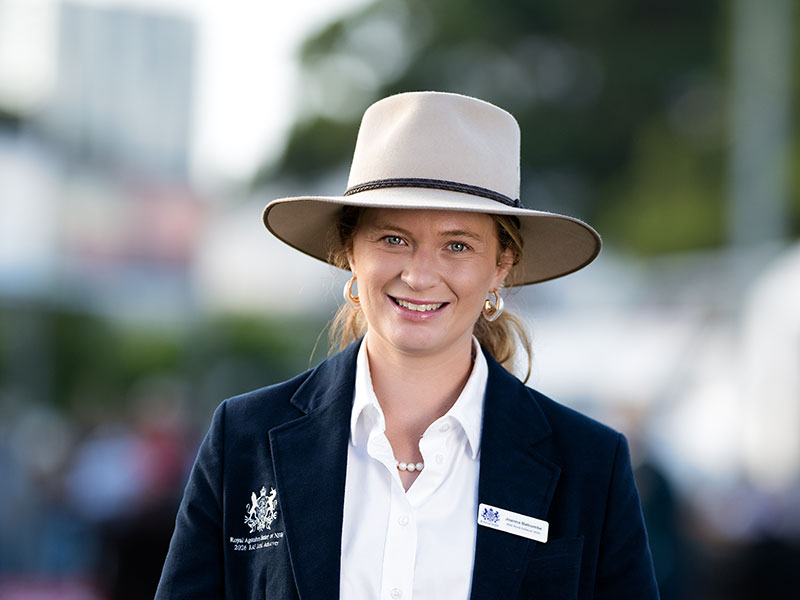 Headshot of 2026 RAS Rural Achiever finalist Joanna Balcombe, a young woman with blonde hair pulled back wearing a wide-brim hat in a navy blazer.