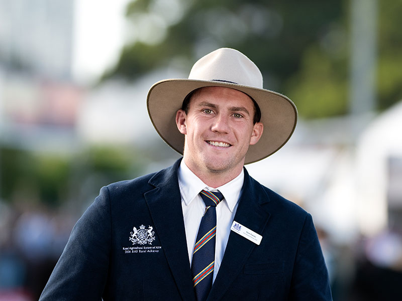 Headshot of 2026 RAS Rural Achiever Sam Parish, a young man with short hear wearing a wide-brim hat and tie in a navy blazer.