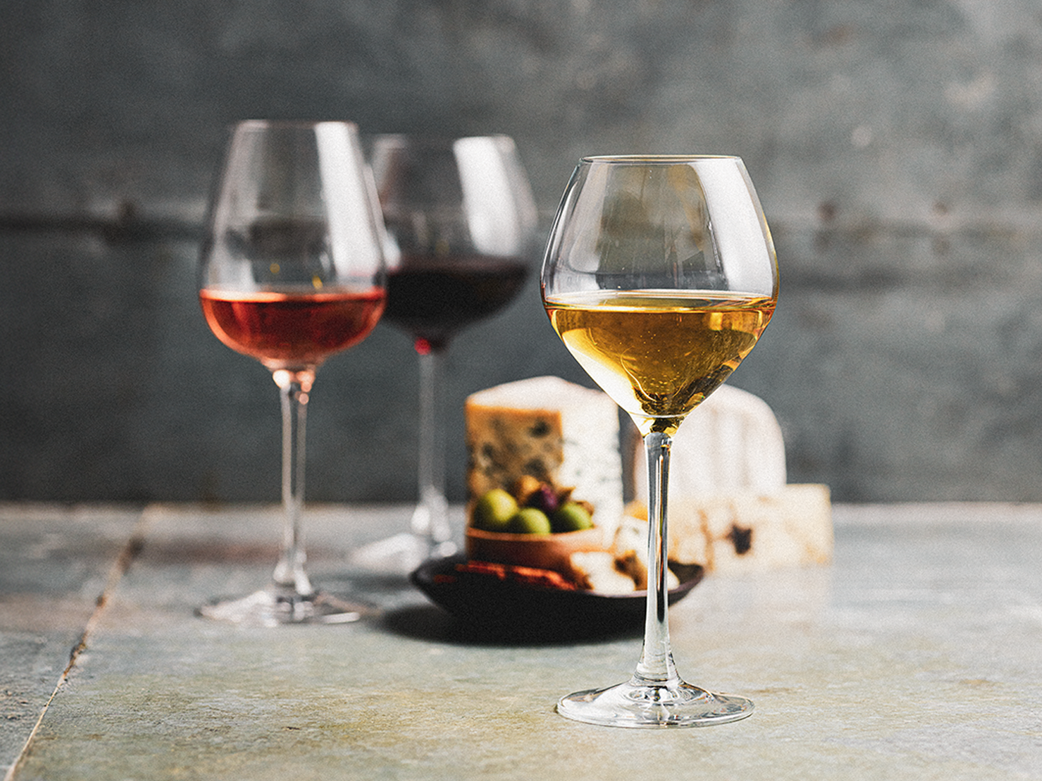 Three glasses of white, rosé, and red wine with cheese and olives in background at the Sydney Royal Wine Show.