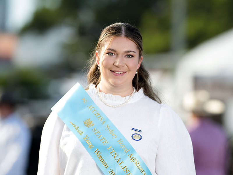 Headshot of 2026 Young Woman finalist Charlotte Moriarty, a brunette woman with hair parted at the centre, wearing a white shirt and a light blue sash.