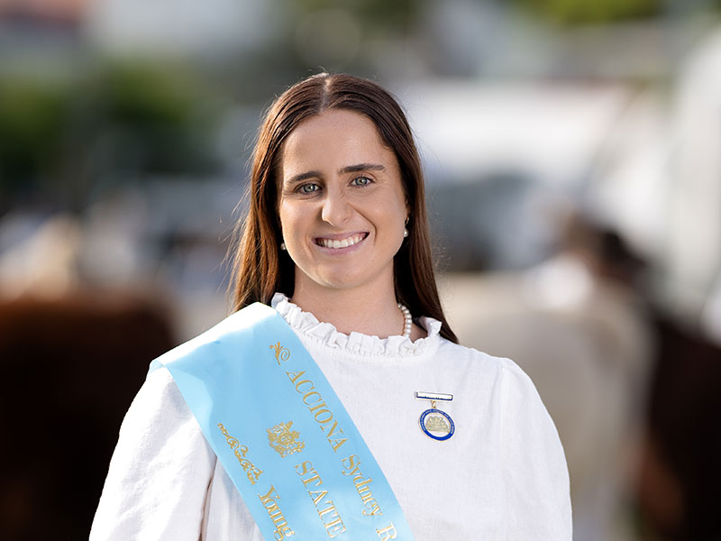 Headshot of 2026 Young Woman finalist Clair Stiff, a brunette woman with long dark hair, wearing a white shirt and a light blue sash.