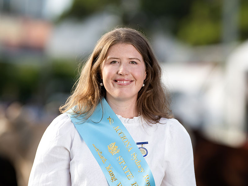 Headshot of 2026 Young Woman finalist Georgia Moody, a woman with long hair parted at the centre, wearing a white shirt and a light blue sash.