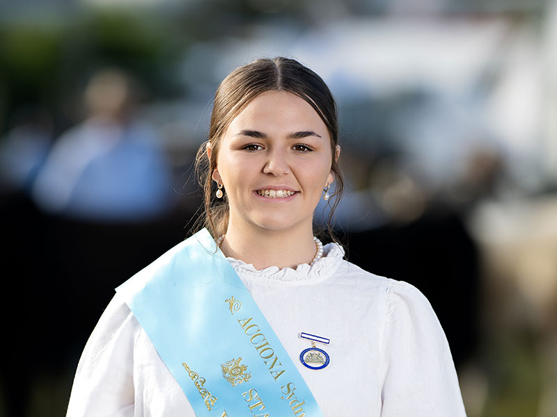 Headshot of 2026 Young Woman finalist Kate Hepburn, a woman with dark hair tied back, wearing a white shirt and a light blue sash.