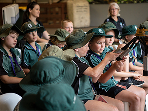 Primary school students in green uniforms and hats examining farm equipment during a Farm Day Excursion.