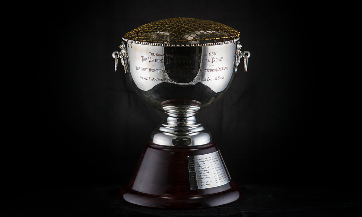 Silver rose bowl with decorative drop handles and wire top, raised on a timber base. First presented in 1958.