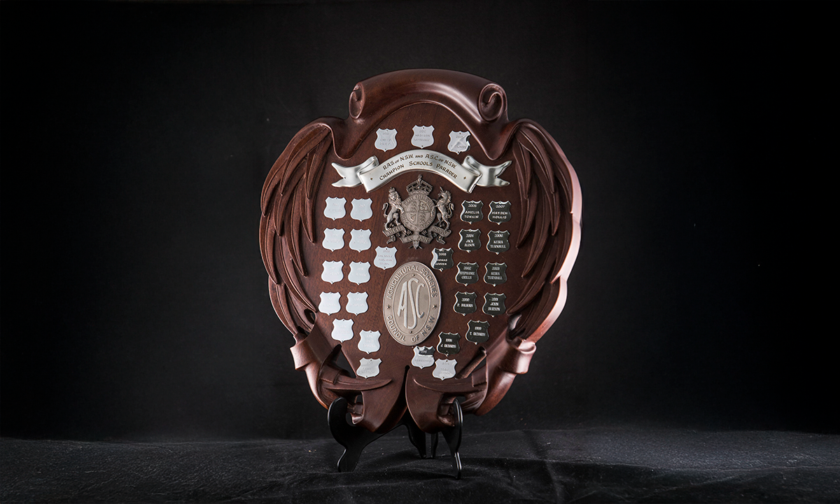 Carved timber shield (oval with gum leaf edge) with crests of RAS & ASC (Agricultural Societies Council). First presented in 1988.