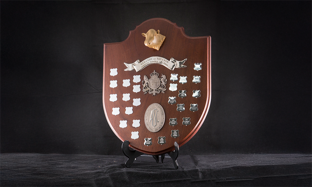 Carved timber shield (oval with gum leaf edge) with crests of RAS & ASC (Agricultural Societies Council). First presented in 1988.