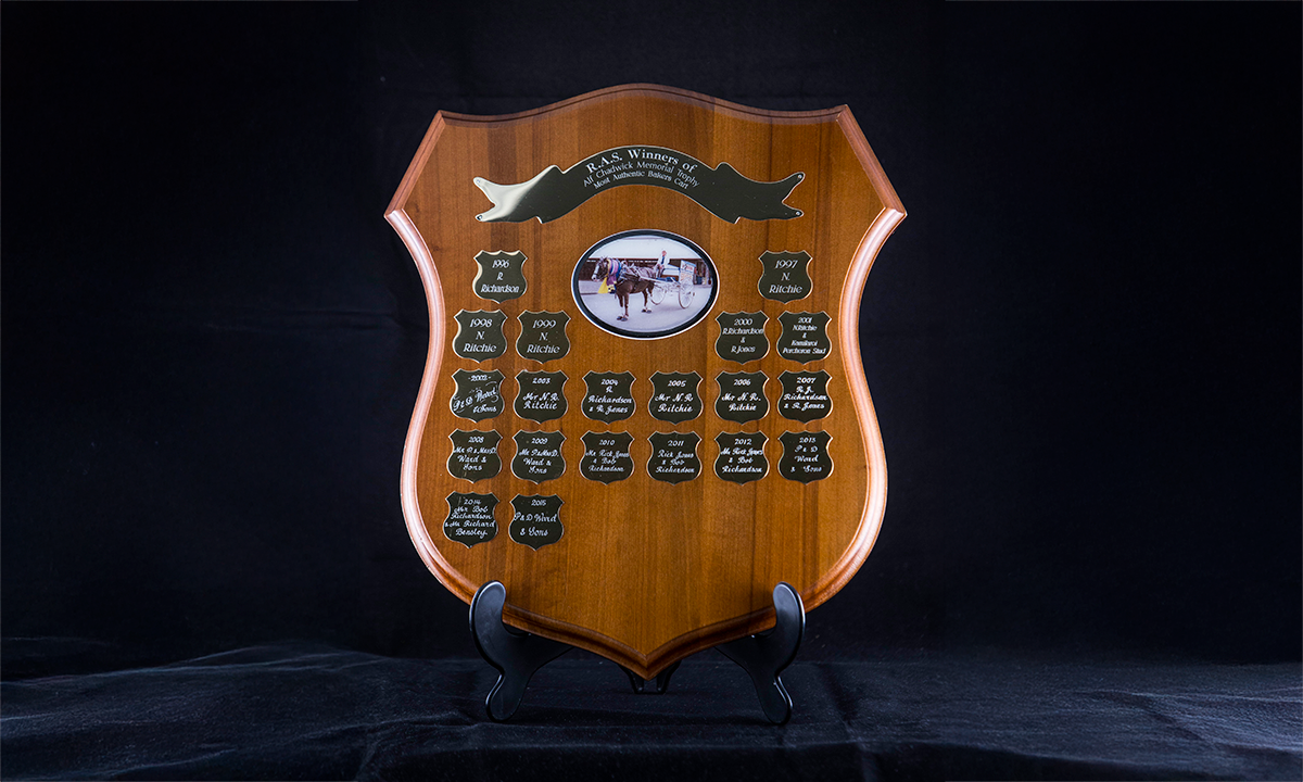 Timber shield with a laminated photograph of a baker's horse and cart affixed to the centre. First presented in 1996.