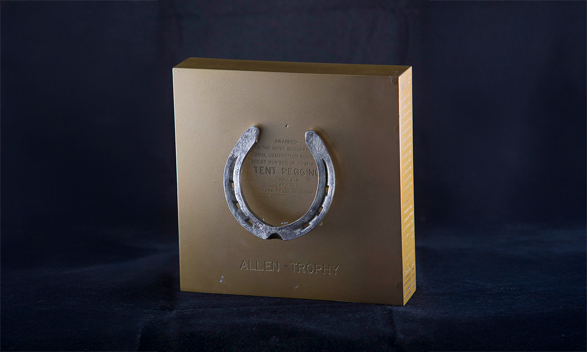 Gold coloured square plaque with a horseshoe mounted on the front. First presented in 1974. 