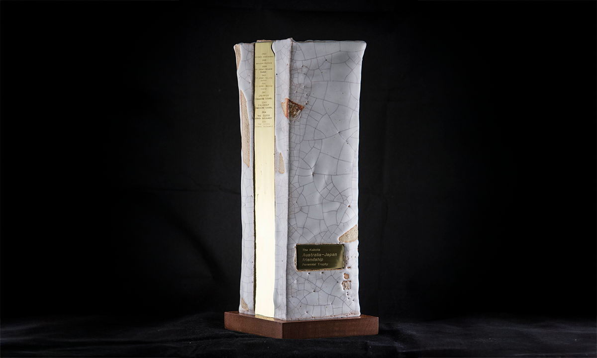Tall ceramic piece on a wooden base. The ceramic is light in colour with pieces of light brown included, along with visible cracking. A narrow gold plate runs the height of the ceramic. First presented in 2007. 