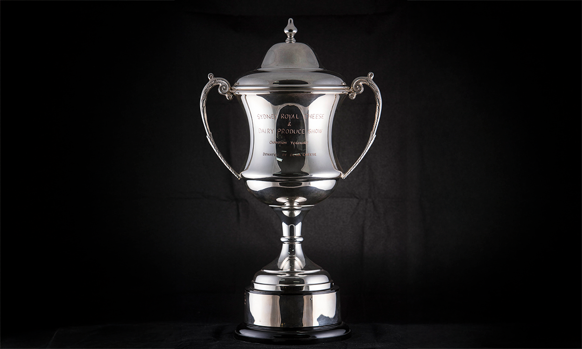 A silver twin handled trophy cup with domed lid, finial and foliate cast handles, raised on a circular base. First presented in 2002. 