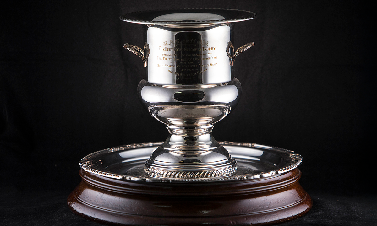 Silver cup with twin handles attached on a circular salver plate base, which is mounted to a circular wooden base. Awarded since 1963.
