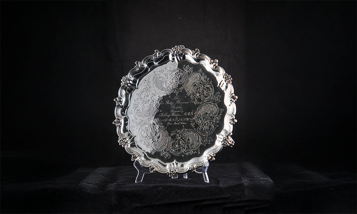 Round silver plate with decorated edges and etched design on surface. The name of the trophy is engraved on the centre of the plate. First presented in 1984.