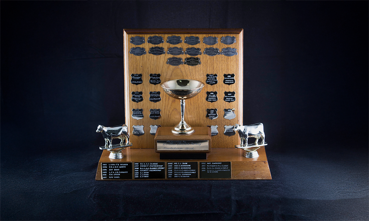9ct gold cup flanked by two gold-plated figures of cows, raised on a tiered oak plinth, backed by a upright piece of wood. First awarded in 1961.