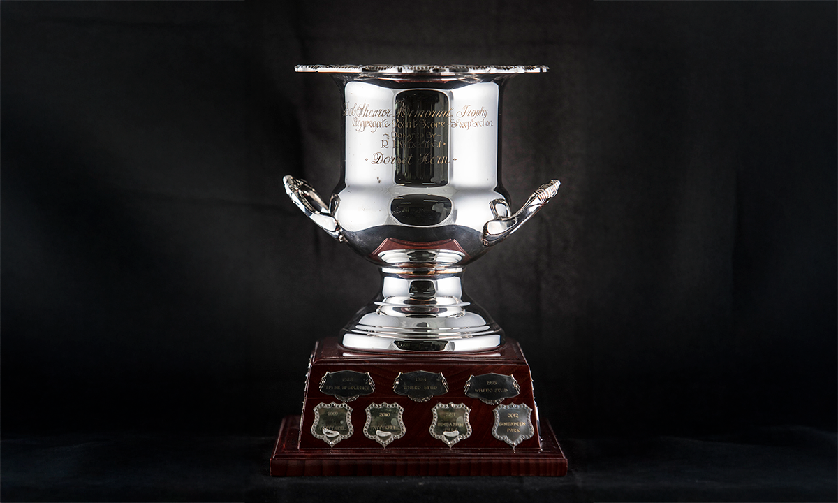 Silver twin handled wine cooler with foliate handles, mounted on a square wooden base with applied presentation shields bearing the names of previous winners. First awarded in 1993.