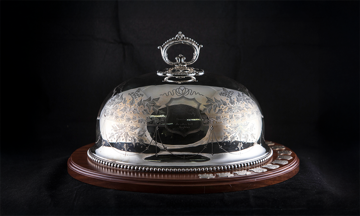 Silver cloche decorated with engraved foliage, and a single scroll handle, mounted on a thin wooden base. First awarded in 2001.