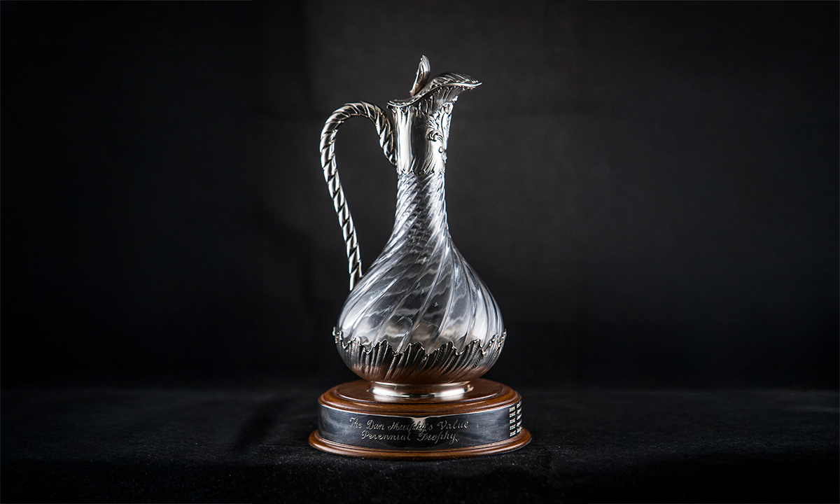 A clear glass wine jug with a swirl moulded body, a rope twist handle and foliate cast mounts on the base. The jug is mounted on a thin oak base with applied sterling silver band. First awarded in 2004.
