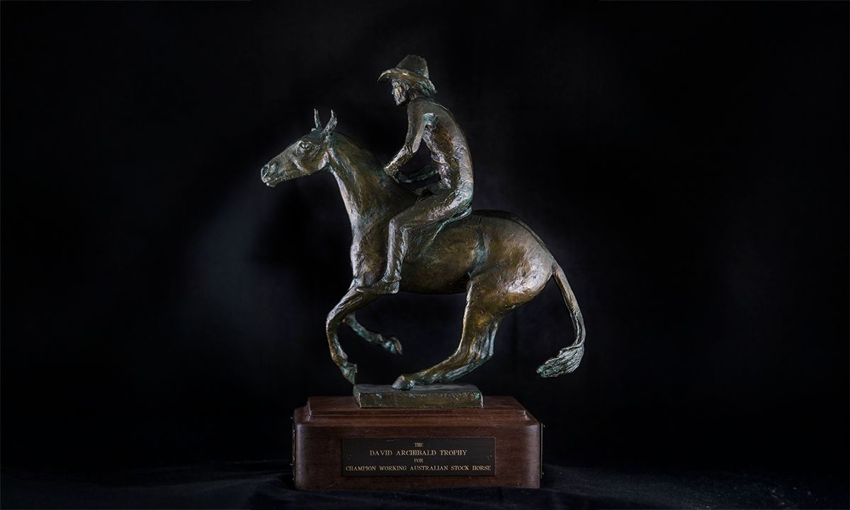 Dark bronze horse and rider with hat, raised on a timber plinth. First presented in 1996. 
