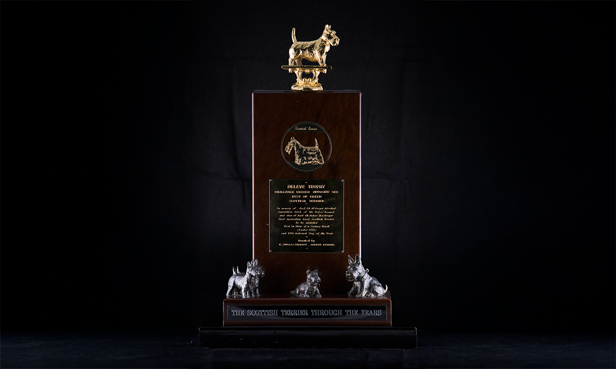 Applied cast metal models of terriers, on a walnut plinth. Titled 