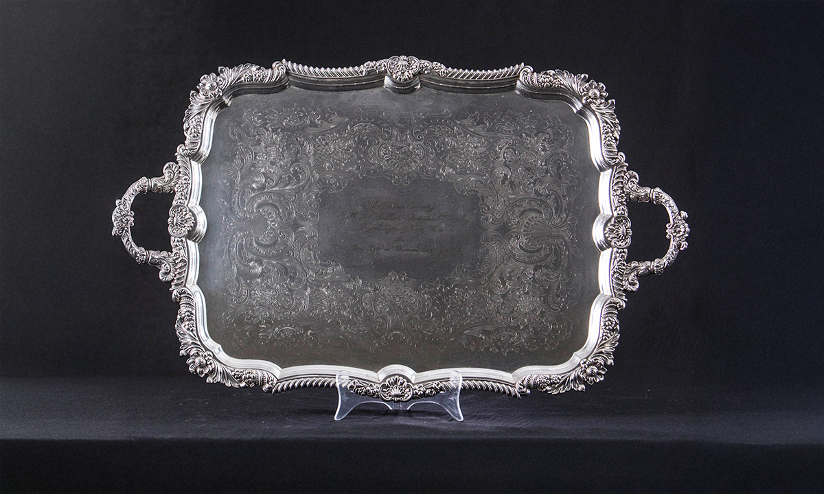 Elaborately engraved rectangular silver plate with decorative border and two foliate handles. First awarded in 1956.