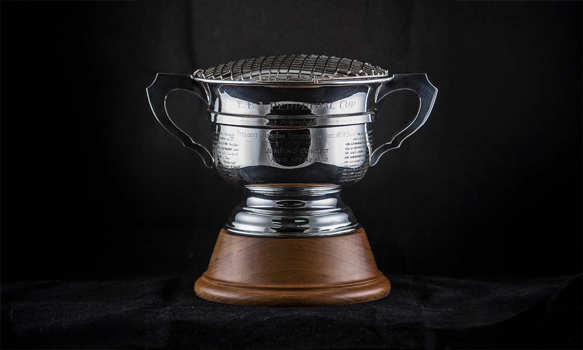 Twin handled silver rose bowl with a wire cover, raised on a circular sloped timber base. First presented in 1951.