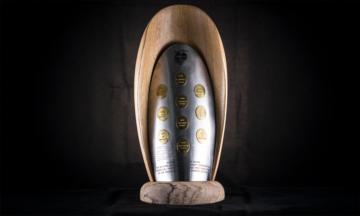 Trophy of abstract design in oak, stainless steel and brass, arched with applied brass medallions, raised on a circular foot. First awarded in 1998. 