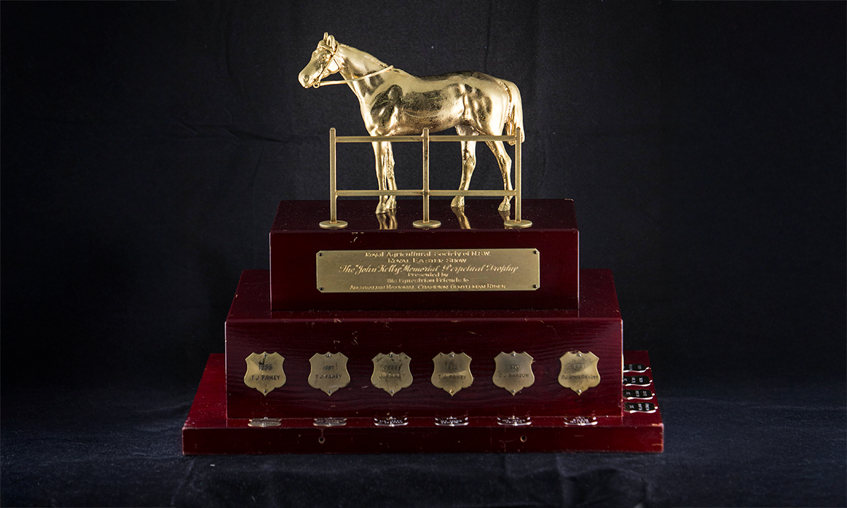 A gold horse and fence, raised on a three-tiered pine rosewood finished plinth, with individual gold name and engraving plates. First presented in 1986. 