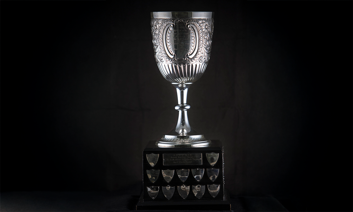 Silver chalice embossed with flowers and foliage, raised on a timber plinth. First presented in 1961.