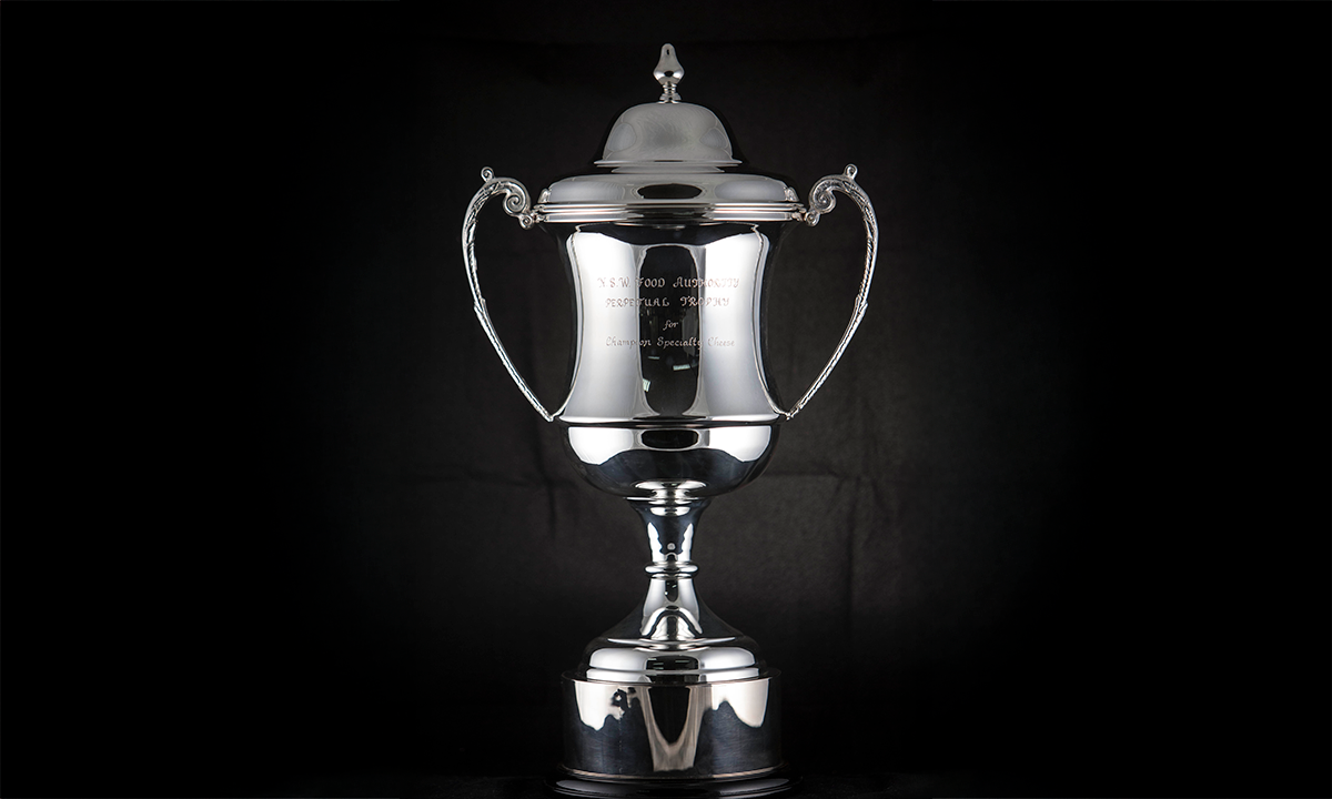 Silver-plated twin handled trophy cup with a domed lid and scroll handles, raised on a black base. First awarded in 2001.