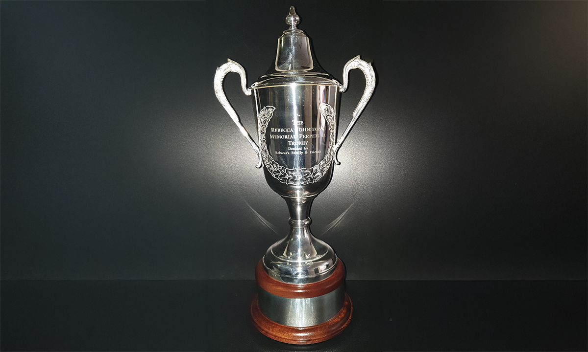 Silver trophy cup with hand chased laurel pattern featuring a mahogany plinth and silver engraving band. First awarded in 2021.