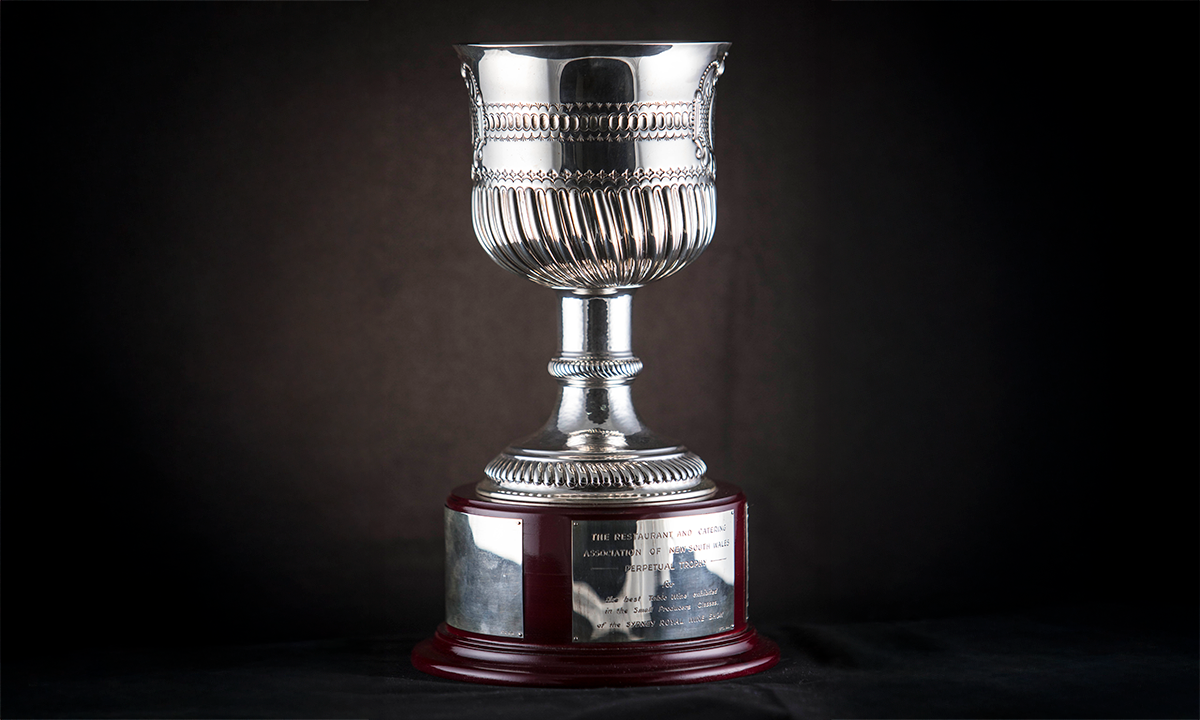 Silver chalice with decorative motifs and border patterns applied, raised on a narrow stem, mounted on a wooden plinth with engraving plates attached. First presented in 1994. 