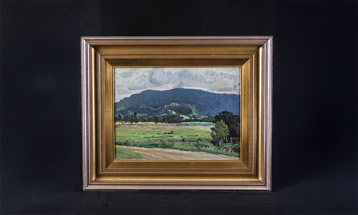 A painting of a rural scene with light cloudy sky, dark green rolling hills, lighter green fields and a sandy-coloured road in view. The painting is set in a gold-coloured frame. First presented in 1984. 