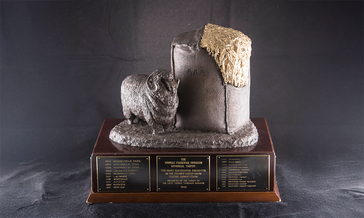 Bronze figure of a Merino Ram standing beside a wool bale with gold wool bursting from it, raised on a rectangular dark wood base. Several engraving plates are attached to the outside of the base. First awarded in 1992.
