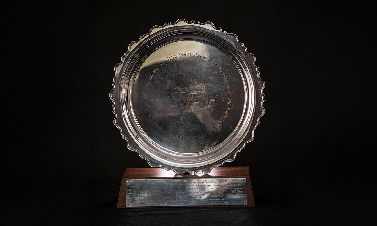 Silver plate engraved with a horse and sulky to the centre, nested in a small groove in wooden plinth. First awarded in 1979.