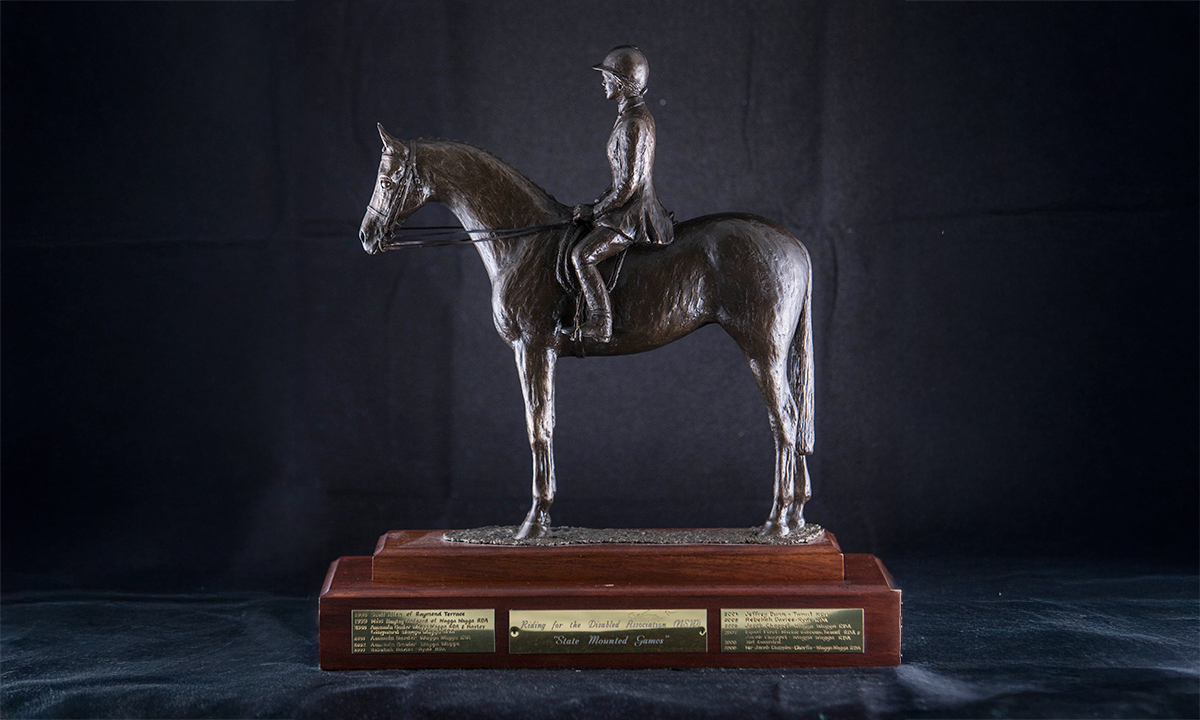 Cold cast bronze model of a horse and rider, raised on a tiered rosewood base with gold-plated labels. First awarded in 1998.