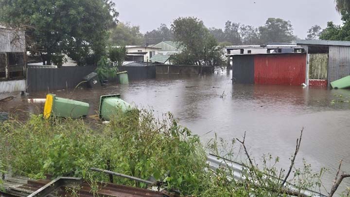 Flooded Taree Showground with submerged sheds, fences and floating debris.