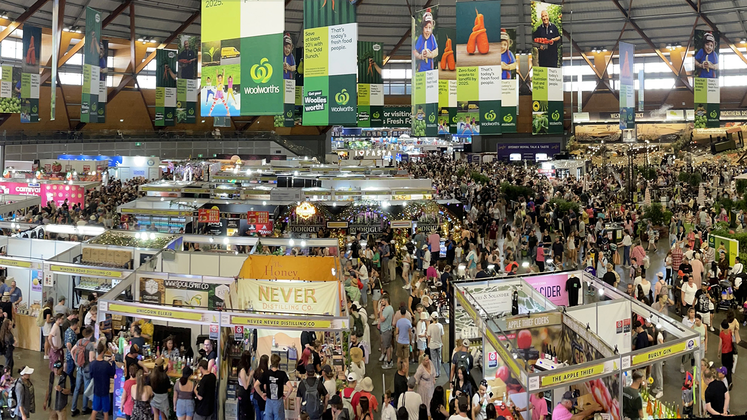 Large crowd exploring exhibition stalls inside the Dome decorated with bright sponsor banners, at the Sydney Royal Easter Show.