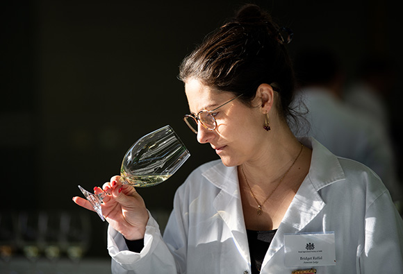 A judge in a white coat and glasses  carefully inspecting a glass of white wine at the Sydney Royal Wine Competition.