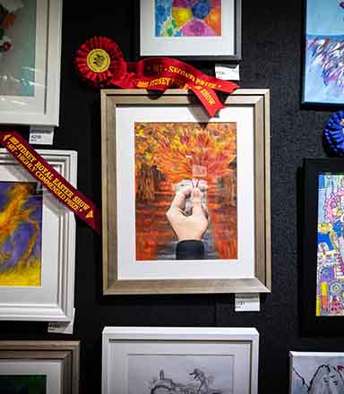 A group of paintings awarded with ribbons, hung against a navy blue wall at the Sydney Royal Arts & Crafts Competition.
