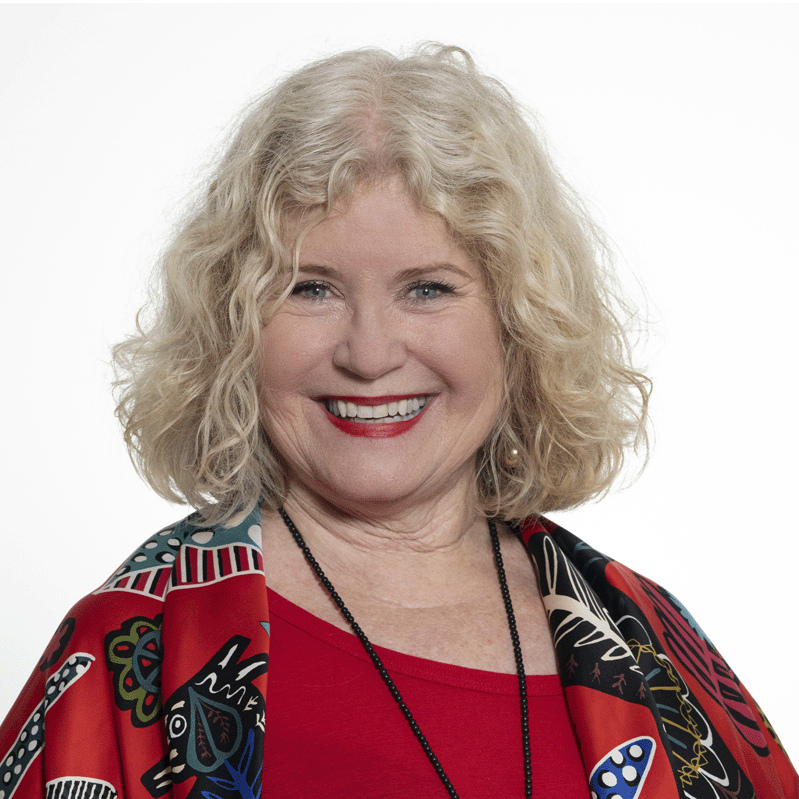 Headshot of Board Member Sally Evans, smiling and wearing a colourful patterned shawl over a red top.